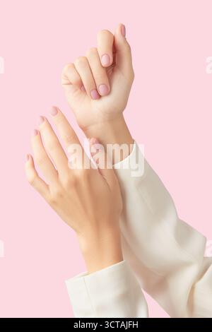 Belles mains de femmes soignées avec un design d'ongle rose mat sur un fond rose Banque D'Images