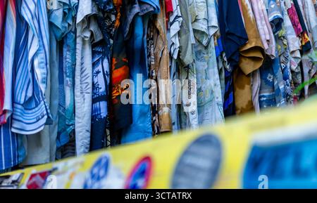 Gros plan de chemises hawaïennes vintage colorées suspendues dans un magasin de seconde main à Berlin Prenzlauer Berg, avec banc autocollant devant. Banque D'Images