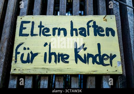 Gros plan d’une enseigne en bois jaune rustique avec texte allemand peint à la main “Eltern haften für ihre Kinder” sur une clôture en bois. Banque D'Images