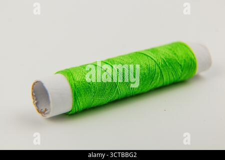 Une bobine verte vibrante de fil à coudre repose sur un fond neutre, prêt à être utilisé dans divers projets d'artisanat et de broderie à tout moment. Banque D'Images