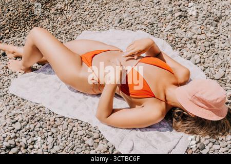 Chapeau de bikini plage de bain de soleil femme - Une femme dans un bikini bains de soleil sur une plage, portant un chapeau pour la protection solaire. Banque D'Images
