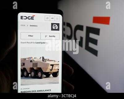 Dans cette illustration photo, une personne tient un téléphone portable avec la page Web de la société de défense émirati Edge Group PJSC sur l'écran devant le logo. Banque D'Images