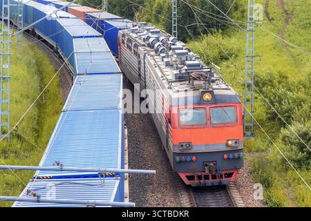 Un train de locomotives de chemin de fer rouge avec des conteneurs d'expédition monte à côté d'un train parallèle également avec des conteneurs de fret bleus parmi les collines verdoyantes vue en gros plan Banque D'Images