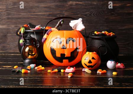 Citrouilles décoratives et chaudrons avec différents bonbons sucrés sur une table en bois noir. Célébration d'Halloween Banque D'Images