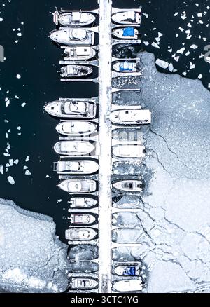 Vue aérienne des bateaux amarrés le long d'un quai au milieu des eaux glacées, le blanc dur de la glace contrastant avec le bleu profond de la mer, créant une scène hivernale fascinante, Svolvaer, Nordland, Norvège. Banque D'Images