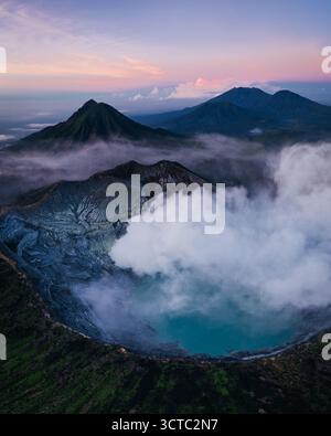 Vue aérienne du volcan éthéré Ijen, où les eaux turquoises rencontrent des panaches de fumée sulfureuse sous un ciel pastel, Mt. Ijen, Jawa Timur, Indonésie. Banque D'Images