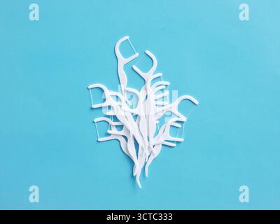 Pics de fil dentaire blanc regroupés sur un fond bleu, représentant des outils essentiels pour maintenir des dents et des gencives saines Banque D'Images
