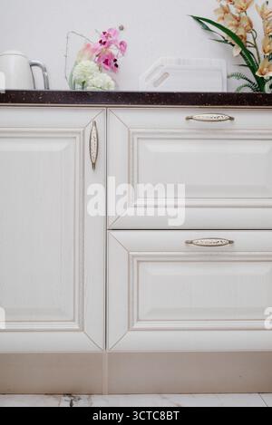 Un fragment d'une cuisine blanche classique avec des armoires effet bois et des accessoires décoratifs en or Banque D'Images