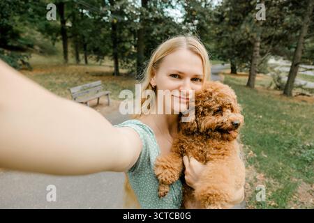 Femme prenant selfie avec caniche dans le parc Banque D'Images