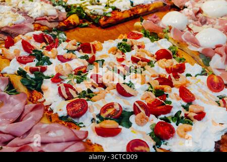 Vue rapprochée de pizza italienne al taglio garnie de crevettes, tomates cerises, roquette et mozzarella exposées dans un comptoir en Italie Banque D'Images