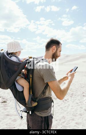 Garçon en bas âge assis dans un porte-sac à dos de randonnée pendant une randonnée Banque D'Images