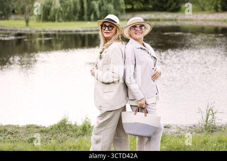 Deux amies âgées heureuses souriant ensemble à l'extérieur dans le parc, dames retraitées portant des vêtements légers, appréciant l'amitié, le bien-être, le vieillissement actif, Banque D'Images