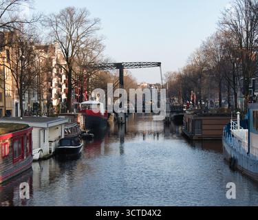 Pont-levis historique d'Amsterdam et péniches - vue emblématique sur un large canal d'Amsterdam avec un pont-levis traditionnel en métal, houseboa résidentiel Banque D'Images