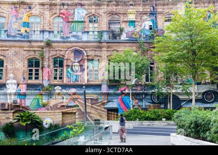 Femme marchant sur le chemin moderne à côté du bâtiment avec une grande murale culturelle d'art de rue Banque D'Images