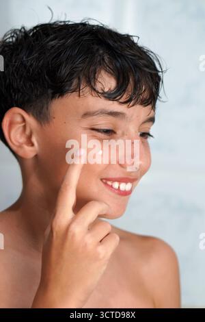 Changements hormonaux, soins de la peau et adolescence. Preteen Boy appliquant un gel desséchant à un bouton d'acné. Banque D'Images