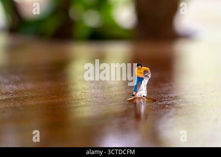 Figurine miniature verse de l'eau sur une surface en bois réfléchissante, mélangeant créativité ludique et narration imaginative dans une scène macro fantaisiste. Banque D'Images