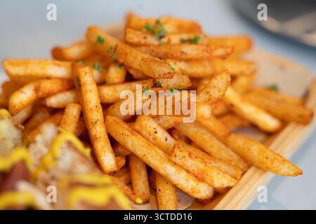 Frites assaisonnées croustillantes dorées servies sur un plateau en bois, saupoudrées d'herbes et d'épices, Banque D'Images