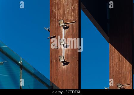 Mélange urbain saisissant : trois projecteurs extérieurs sur une poutre en bois altérée contre un ciel bleu éclatant, combinant des éléments modernes et rustiques pour un développement durable Banque D'Images