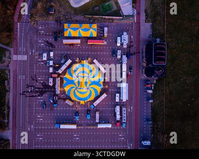 Vue aérienne de la configuration vibrante de cirque dans le parking tente en spirale jaune bleu entouré de remorques et de tentes plus petites, mettant en valeur la logistique organisée an Banque D'Images