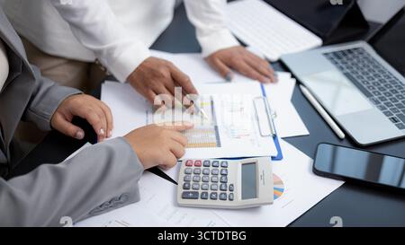 Gros plan de deux femmes d'affaires analysant des graphiques et des données financières à l'aide d'une calculatrice et d'un ordinateur portable dans un bureau moderne. Concept de travail d'équipe, planification financière, Banque D'Images