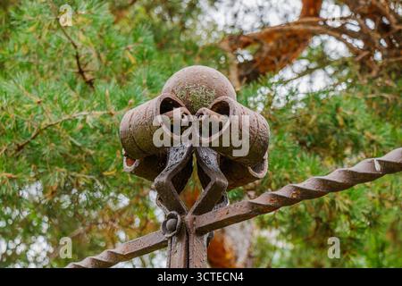 Vue détaillée d'un finial décoratif en fer forgé avec des éléments recourbés et texturés, montrant la rouille et la patine, sur fond naturel de Gree Banque D'Images
