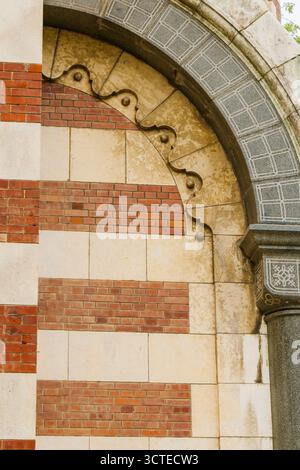 Vue détaillée d'un mur de bâtiment historique composé d'une alternance de briques rouges et de blocs de pierre, avec un motif de maçonnerie voûtée orné et géométrique Banque D'Images