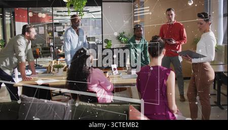 Équipe collaboratrice de collègues discutant de stratégie dans un bureau ouvert, avec moniteur et verdure Banque D'Images