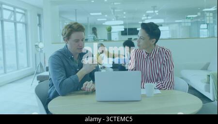 Collaborateurs tenant une tasse et tapant sur un ordinateur portable argenté dans un bureau moderne, avec des tasses blanches Banque D'Images