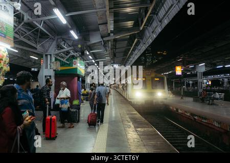 Mumbai, Inde - 23 septembre 2025 : vue sur un quai ferroviaire animé où un train lumineux vous attend, projetant de longues ombres au milieu des navetteurs et des bagages. Banque D'Images