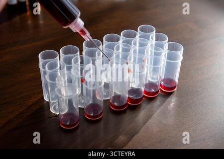 L'invention concerne une personne utilisant une seringue pour injecter une substance dans des rangées de récipients d'échantillons disposés sur un plateau de table. Banque D'Images