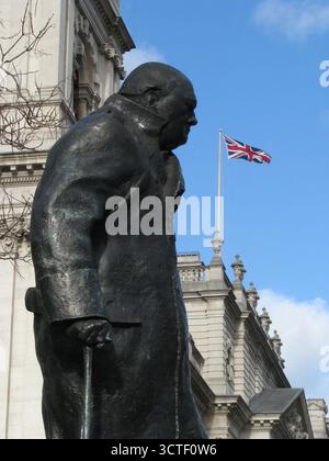 La statue de Winston Churchill se dresse sur la place du Parlement avec les drapeaux de l'Union qui flottent depuis les édifices gouvernementaux emblématiques derrière. Banque D'Images