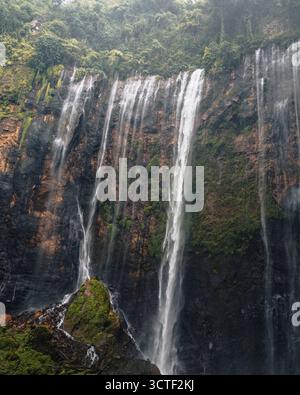 Vue sur les cascades plonger dans une falaise accidentée, enveloppée de brume et de verdure luxuriante, créant un spectacle naturel époustouflant, Tumpak Sewu, Banque D'Images