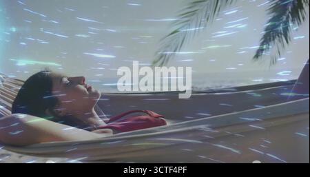 Femme en haut de bikini rouge bronzer dans un hamac à la terrasse du bord de mer, balustrade blanche et frondes de palmier Banque D'Images