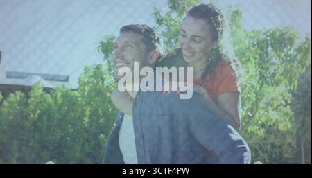 Portant un homme vêtu de denim et une femme au sommet rouge sur porcherie dans la cour arrière, avec des ombres de clôture et des arbustes Banque D'Images