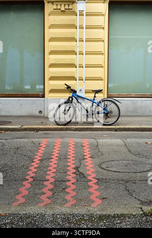 Vevey, Suisse - 24 septembre 2025 : un vélo bleu est garé contre un bâtiment jaune avec des motifs en zigzag rouges sur la route. Banque D'Images