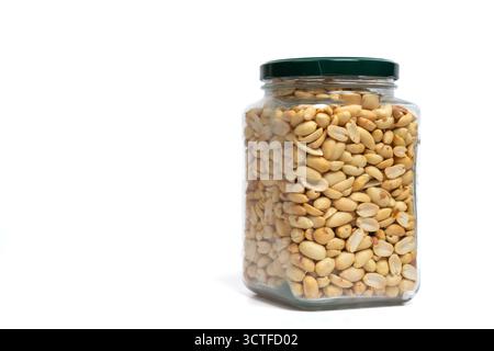 Pot en verre avec couvercle vert rempli d'arachides sur fond blanc isolé. Gros plan du pot rempli de cacahuètes snack. Nutrition, stockage, santé Banque D'Images