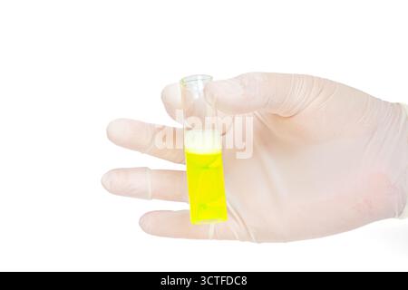 Main gantée tenant tube à essai avec liquide jaune sur fond blanc isolé. Gros plan de la main gantée avec un tube à essai en verre rempli de jaune Banque D'Images