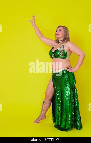 Sensualité femme mature danseuse vêtue dans la tenue de danse - haut vert à paillettes et jupe longue avec fente et elle ne porte pas de chaussures, mouvement dedans Banque D'Images