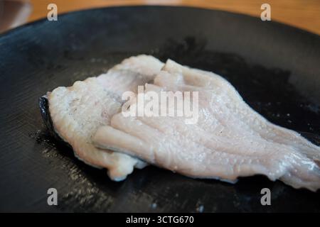 Filets d'anguille crue fraîche sur une assiette noire, prêts pour la cuisson Banque D'Images