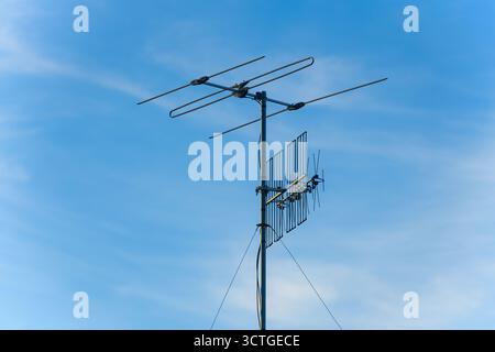 Antenne TV montée sur un poteau métallique contre un ciel bleu clair. Antenne de toit traditionnelle utilisée pour la réception de signaux de diffusion numériques et analogiques. Banque D'Images