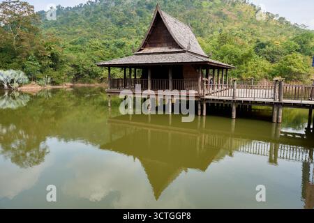 Un bâtiment en bois se dresse sur pilotis au bord d'un lac calme, entouré d'arbres luxuriants et de collines. L'eau sereine reflète la structure et le landsca vibrant Banque D'Images