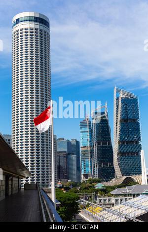 Vue verticale du drapeau national de Singapour agitant en mouvement. Soulevé sur une barre de support ou un poteau. Temps nuageux et ciel bleu. Contre l'hôtel Swissôtel Banque D'Images