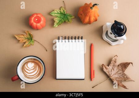 Pose plate d'automne confortable avec café latte art, cahier, stylo, bougie de citrouille et feuilles d'automne sur fond beige. Concept saisonnier chaleureux, vue de dessus, maquette Banque D'Images