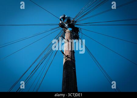 Poteau télégraphique avec de nombreux fils rayonnants contre un ciel bleu clair Banque D'Images