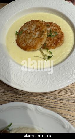 Purée de pommes de terre avec deux galettes panées garnies de microgreens sur une assiette blanche ornée. Photo mobile Banque D'Images