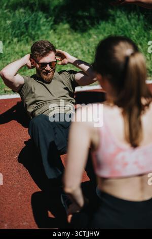 Homme effectuant des sit-ups à l'extérieur avec les conseils d'une femme pendant la journée ensoleillée Banque D'Images