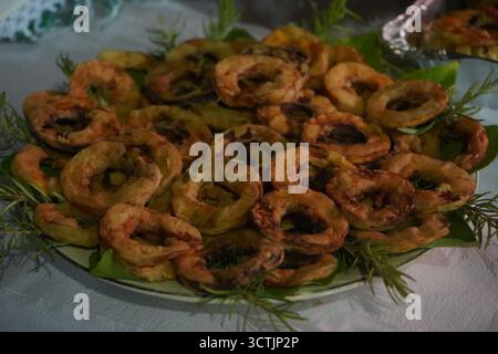Une assiette d'anneaux de citrouille frits, légèrement battus et dorés, magnifiquement garnis de brins de romarin frais, capturés lors d'un festival nocturne en Crète. Banque D'Images