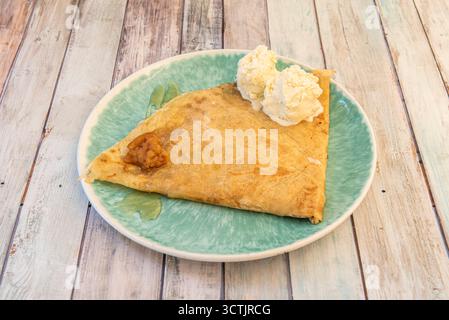 Crêpe avec sucre glace, crème glacée à la vanille et tarte aux pommes avec sirop sur une assiette verte Banque D'Images