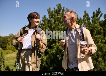 Couple senior randonne à travers une végétation luxuriante, partageant des sourires et profitant de leur aventure. Banque D'Images