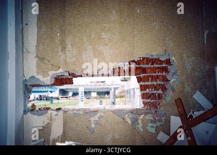 Trou carré dans le mur extérieur d'une usine abandonnée avec du papier peint, montrant l'extérieur, capturé dans un film flash analogique. Banque D'Images